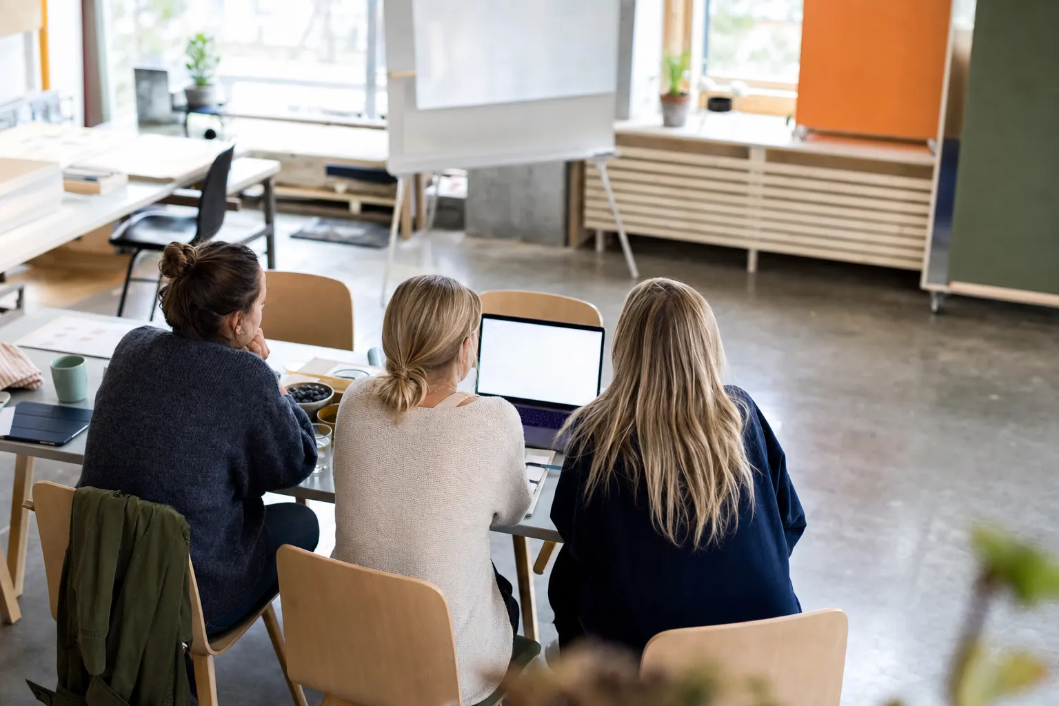 En liten grupp, sedd bakifrån, samlad kring en laptop i ett ljust nordiskt workshoprum under en onboarding-session.