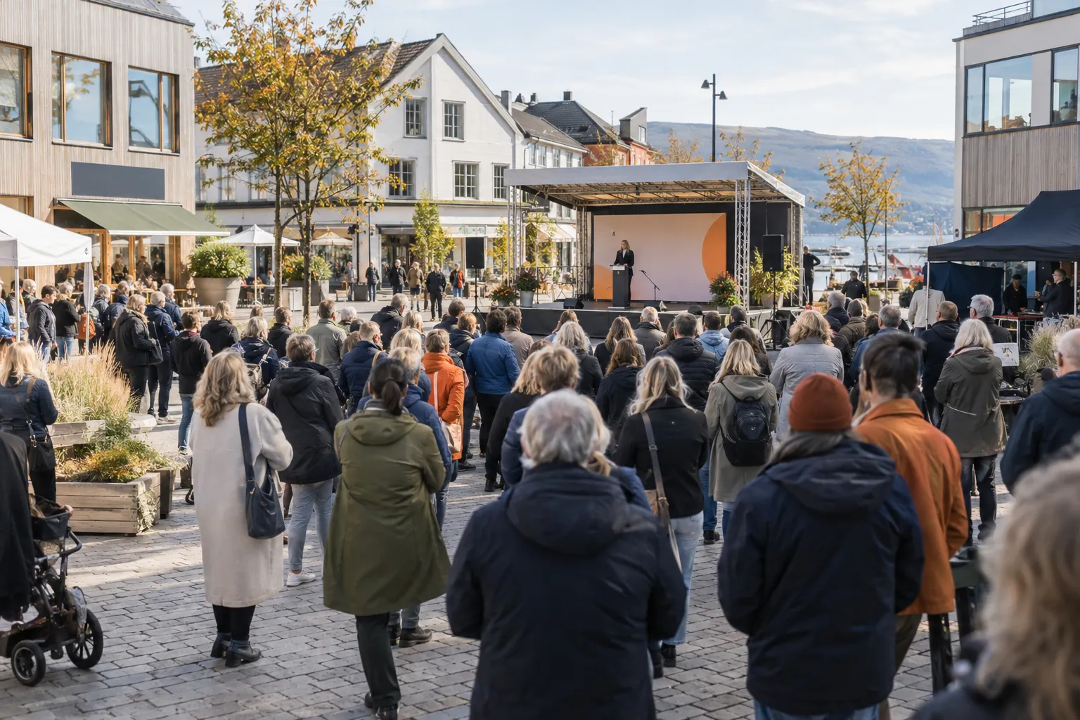 Publikum på et kampanjearrangement på et torg omgitt av butikker